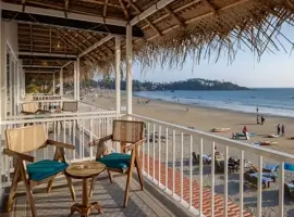 A serene beachfront balcony adorned with elegant chairs and tables, offering a breathtaking view of the sandy beach and azure waters, where one can unwind and embrace the soothing ocean breeze.
